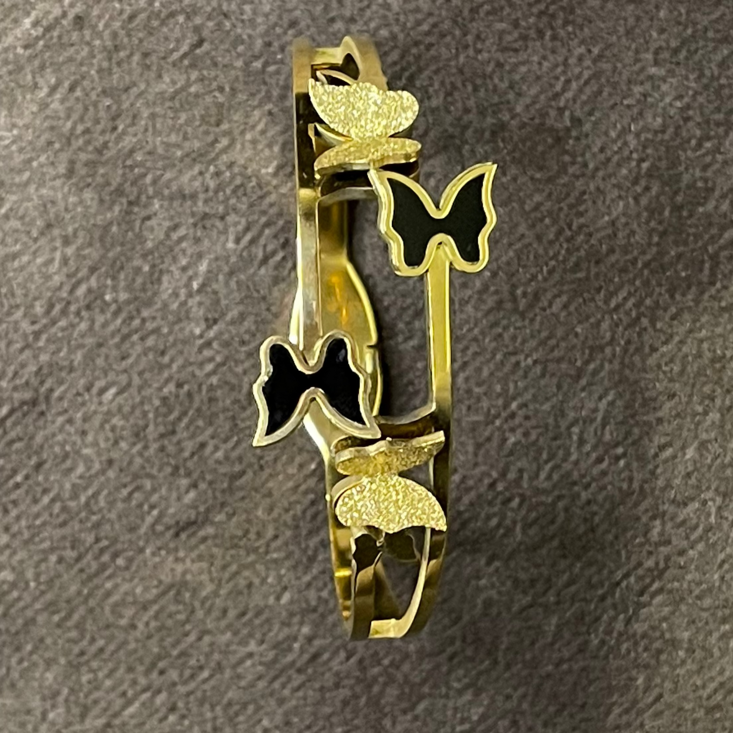 Bangle with white and black enamel butterflies and textured golden butterflies,displayed on a dark surface.