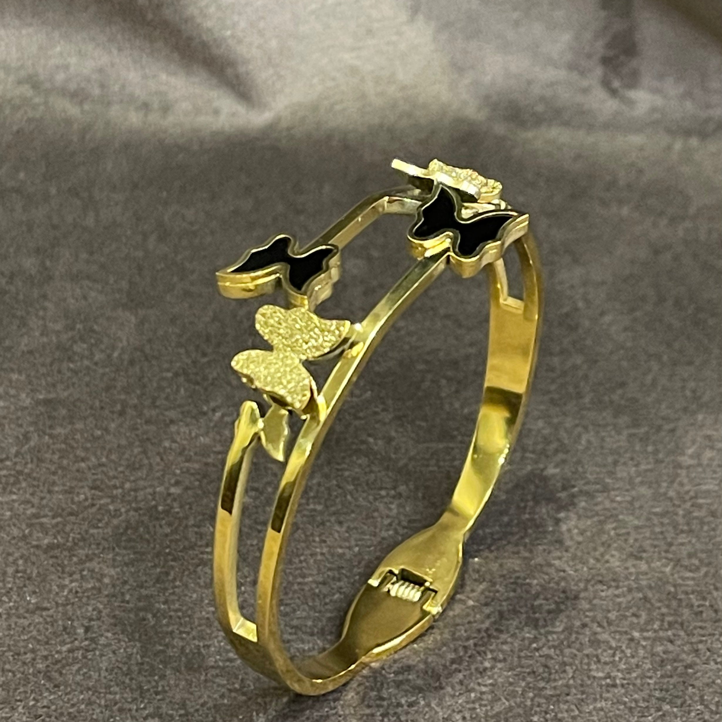 Bangle butterfly designs,with black and white enamel butterflies and textured golden butterflies,displayed on a dark surface.
